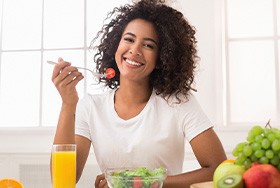 Woman with curly brown hair eating a salad with a glass of orange juice