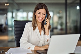 Smiling woman talking on phone and working on laptop