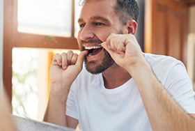 Man smiling while flossing his teeth in bathroom