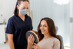 Patient smiling at reflection in mirror with dental assistant