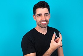 Man in black shirt holding Invisalign with blue background