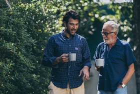 Two men talking on a walk while holding coffee mugs