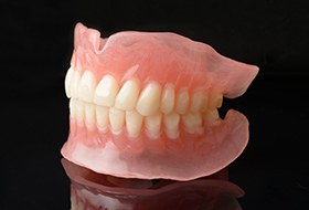 Profile view of a full set of dentures on a reflective black surface