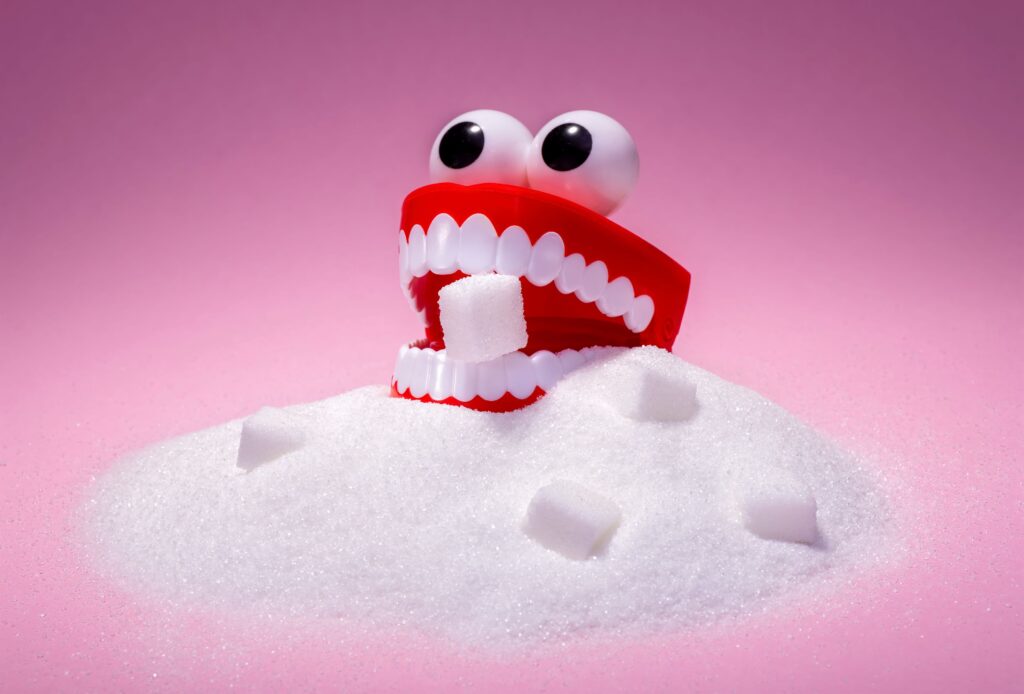 Toy teeth with eyes in a pile of sugar eating a cube with pink background